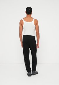 Μαύρο παντελόνι φόρμας με στενές μπατζάκια και λευκό κείμενο στο πλάι. Συνδυάζεται με λευκό αμάνικο μπλουζάκι. Η μέση έχει λάστιχο και υπάρχει μια πίσω τσέπη.