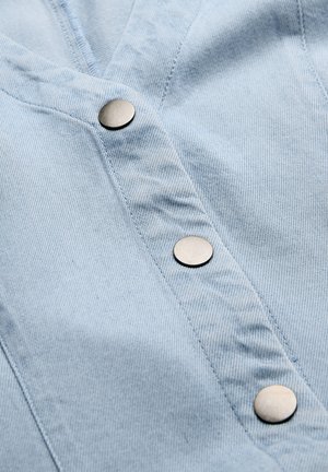 Lichtblauwe denimstof met drie ronde zilveren drukknoopjes die verticaal op een kledingsluiting zijn uitgelijnd.