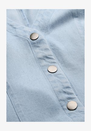 Hellblaue Jeansstoff mit drei runden silbernen Druckknöpfen, die vertikal an einem Kleidungsverschluss ausgerichtet sind.