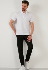 Fehér pólóing texturált felülettel, rövid ujjú, gombos nyitással, fekete, slim fit nadrággal és fehér sportcipővel párosítva.