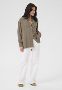 Long-sleeve, button-up shirt in muted olive green, made of smooth fabric. Paired with white wide-leg pants and beige slip-ons.