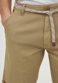 Șorturi khaki dintr-un material durabil, cu un tiv cu model și închidere cu un nasture maro, având buzunare laterale, subliniind un design casual.