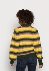 Sweter w paski w odcieniach żółtego, zielonego i brązowego. Dzianinowa faktura z wysokim kołnierzem i ściągaczami przy mankietach. Luźny krój z opadającymi ramionami.