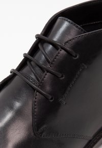 Černé v lesklé kůži vyrobené formální boty se zavřeným šněrováním a detailním prošív�áním na nártu a bočních částech.