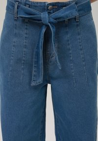 Jeans w średnim niebieskim odcieniu z wiązaniem w pasie, wysoki stan, plisami z przodu oraz klasycznym pięciopocketowym stylem, z eleganckim zapięciem na guzik.