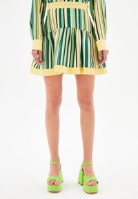 Vestido a rayas verdes y amarillas con vuelo en el bajo, combinado con sandalias de plataforma verde gruesas con correas en el tobillo. Textura suave, diseño casual.