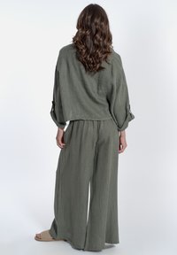 Completo in lino verde oliva, comodo e largo, composto da una camicia corta con maniche risvoltate e pantaloni a gamba larga. Tessuto texturizzato.
