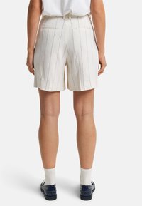 Witte linnen shorts met verticale blauwe strepen, voorzien van twee achterzakken en een losse pasvorm, gedragen met marineblauwe instappers en witte sokken.