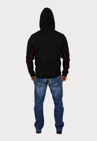 Hanorac negru cu glugă, cu dungi roșii pe lateral, combinat cu blugi albaștri. Imaginea arată spatele, având un design simplu și o croială ajustată.