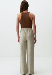 Top in cotone marrone a coste abbinato a pantaloni in lino beige chiaro, larghi e con vita elastica, mostrati da dietro.