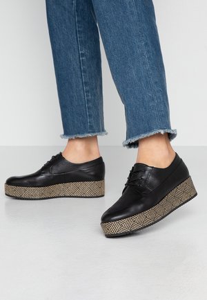 Czarne skórzane buty na platformie z plecioną beżowo-brązową wzorzystą podeszwą klinową. Buty mają gładkie wykończenie i sznurowanie.