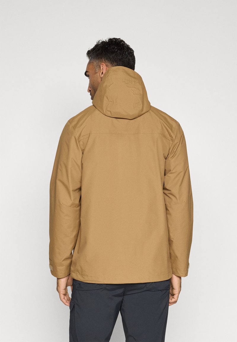 Chaqueta impermeable marrón con capucha, fabricada con un tejido texturizado, bolsillos con cremallera y puños ajustables. Diseño sencillo y funcional para uso al aire libre.