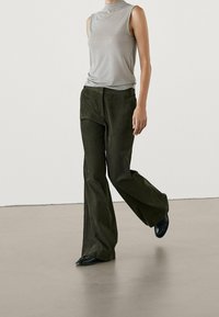 Haut gris sans manches associé à un pantalon évasé en velours côtelé vert foncé. Chaussures noires visibles. Texture lisse ; design simple, sans motifs ni accents.