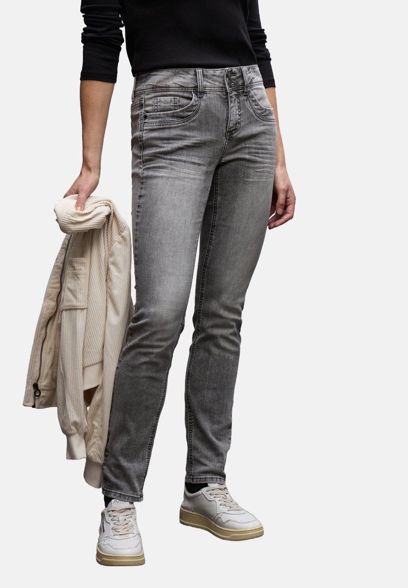 Jeans de denim gris con un corte ajustado, cinco bolsillos y un leve desgaste. Combinados con una chaqueta bomber de color beige claro y utilizados con zapatillas blancas.