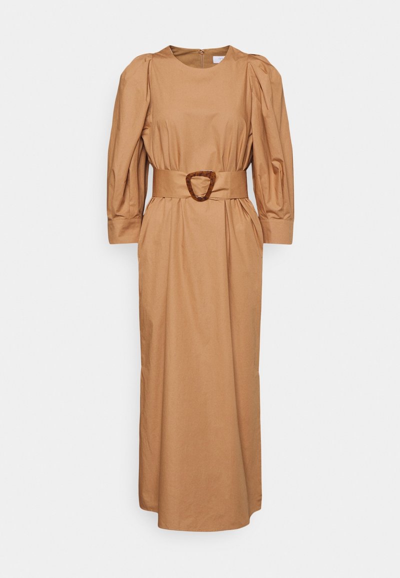 Longue robe beige avec manches longues bouffantes, encolure ronde et large ceinture assortie avec une boucle en écaille de tortue à la taille.