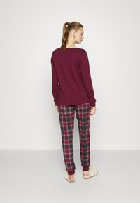 Bordeaux langemouwen top gecombineerd met geruite broek met bordeaux-, marineblauwe en witte accenten. Zachte textuur, aangesloten manchetten en een relaxte pasvorm.