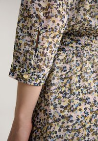 Sukienka w kwiatowy wzór z lekkiego materiału w odcieniach żółtego, różowego i niebieskiego. Posiada podwinięte rękawy oraz dekoracyjny złoty guzik.