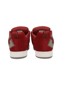 Κόκκινα αθλητικά παπούτσια από σουέντ με επένδυση από μαλακό διχτυωτό υλικό στο εσωτερικό, λευκή λαστιχένια σόλα και έντονο καφέ λογότυπο στην φτέρνα. Εμφανίζεται η πίσω όψη.