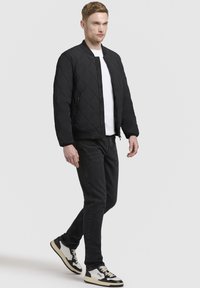 Svart vadderad bomberjacka med dragkedja, bärs över en vit t-shirt, tillsammans med svarta jeans och tvåfärgade sneakers.