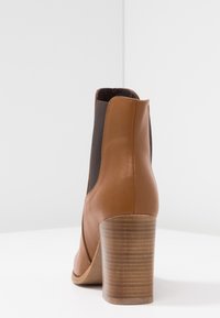 Bota ankle in pelle marrone con pannelli elastici laterali, punta arrotondata e tacco blocco in legno medio con texture rigata.