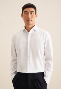 Camicia bianca con colletto a camicia, maniche lunghe e motivo a quadri blu. Il tessuto appare liscio e leggero.