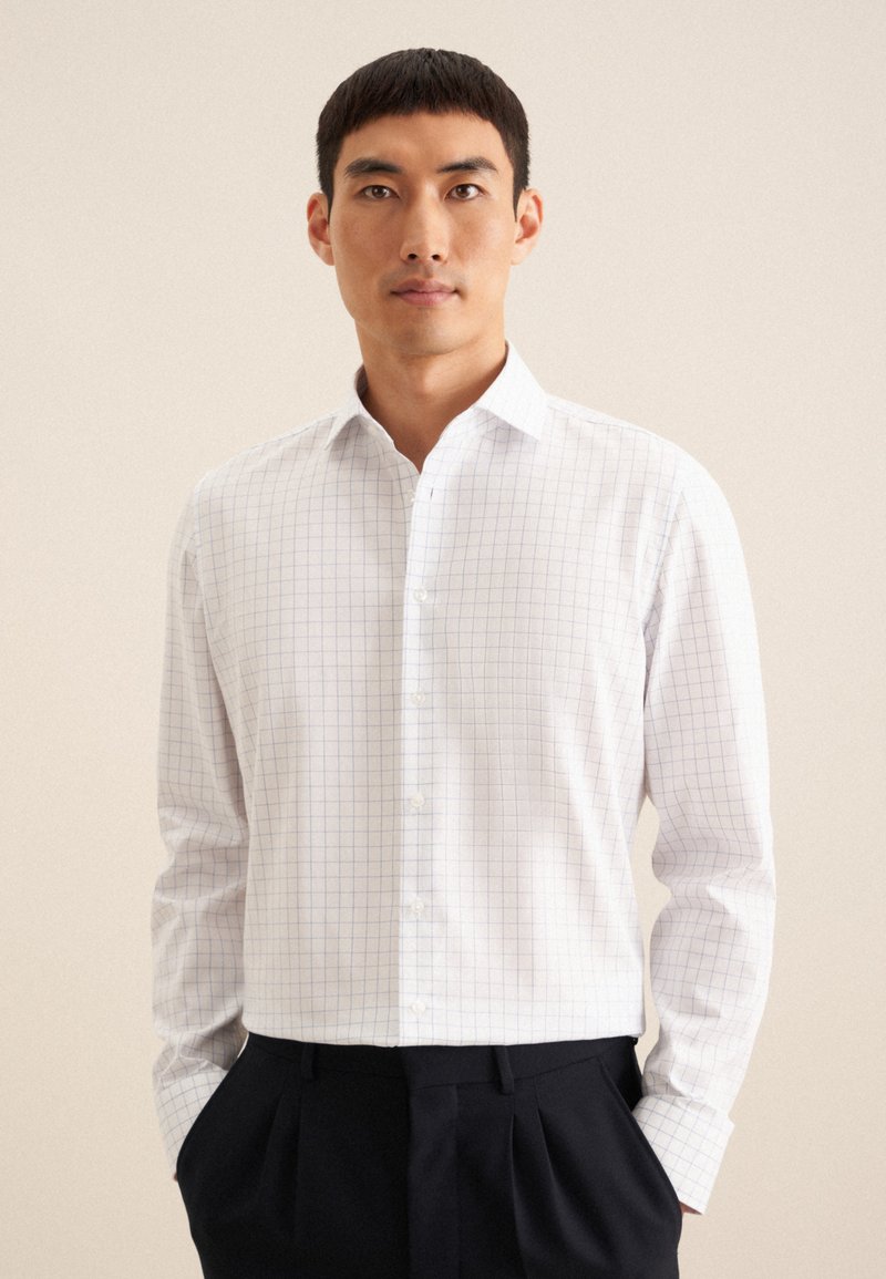 Camicia bianca con colletto a camicia, maniche lunghe e motivo a quadri blu. Il tessuto appare liscio e leggero.