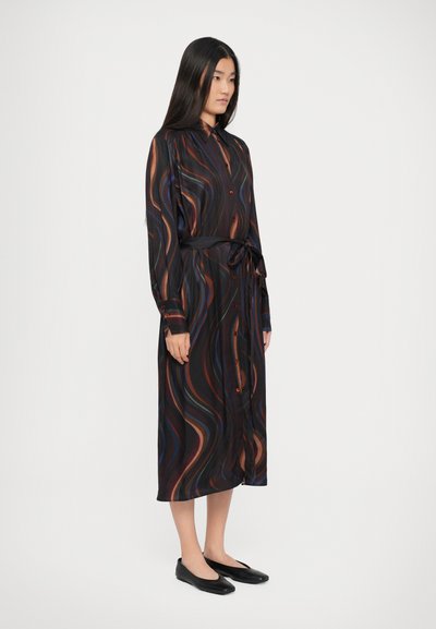 Vestido preto de mangas longas com padrão ondulado colorido, gola, fecho de botão à frente e cinto. O tecido parece leve e suave; combinado com sapatilhas pretas.