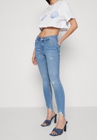 White cropped t-shirt with blue shell design, light blue distressed skinny jeans with ripped hems, and navy high-heeled sandals with studs.