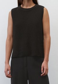 Top senza maniche lavorato a maglia scuro con una texture a coste e scollo rotondo, abbinato a pantaloncini neri larghi.