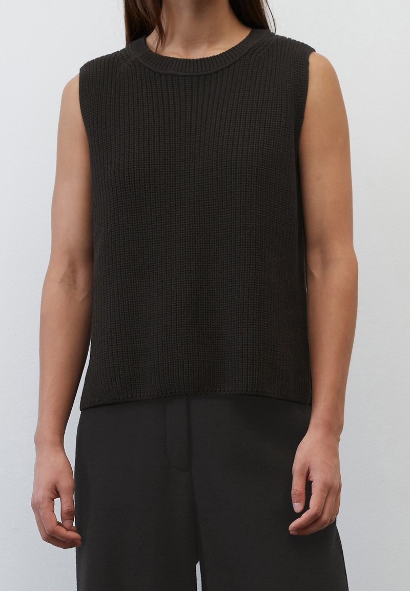 Top senza maniche lavorato a maglia scuro con una texture a coste e scollo rotondo, abbinato a pantaloncini neri larghi.