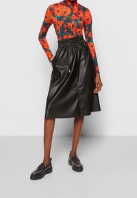 Kvinna som bär en svart midilång läderkjol med elastisk midja och svarta loafers, kombinerat med en röd och blå blommig långärmad topp.