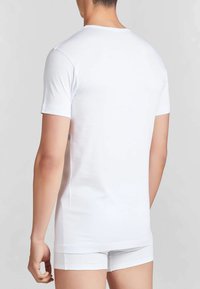 T-shirt bianco a maniche corte realizzato in tessuto morbido, con scollatura tonda e design aderente, indossato con pantaloni corti bianchi coordinati.