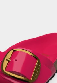 Κοντινό πλάνο ενός ροζ σανδαλιού με μια μεγάλη χρυσή αγκράφα και υφή φελλού στην σόλα που φαίνεται στην άκρη.