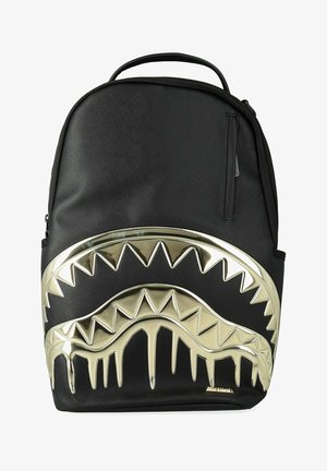 Zaino nero con design di denti dorati lucidi e frastagliati sulla parte anteriore, manico superiore per il trasporto e tasca con cerniera sul lato destro.