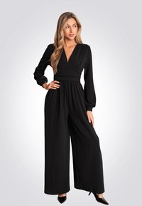 Salopette noire avec de longues manches bouffantes et un décolleté en V profond. La taille est cintrée, menant à un pantalon à jambes larges. Tissu lisse sans motifs.