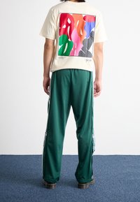 Cream short-sleeve t-shirt featuring a colorful abstract print on the back. Paired with green satin pants and black platform shoes.