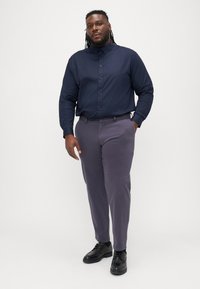 Camicia blu navy con bottoni, maniche lunghe, abbinata a pantaloni grigi scuri e scarpe nere. Tessuto morbido con una vestibilità aderente.