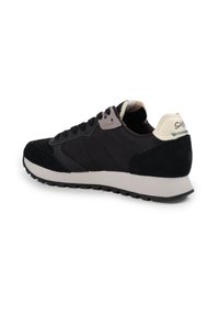 Scarpa sportiva nera in materiale scamosciato e sintetico, presenta una suola curvata, chiusura con lacci, accenti a contrasto grigi e crema sul tallone.