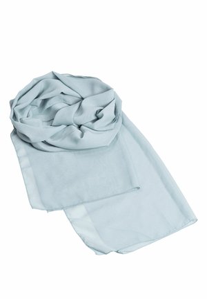 Femme portant une robe sans manches en satin bleu clair avec une fente haute et un col ras du cou, associée à des talons argentés à brides.