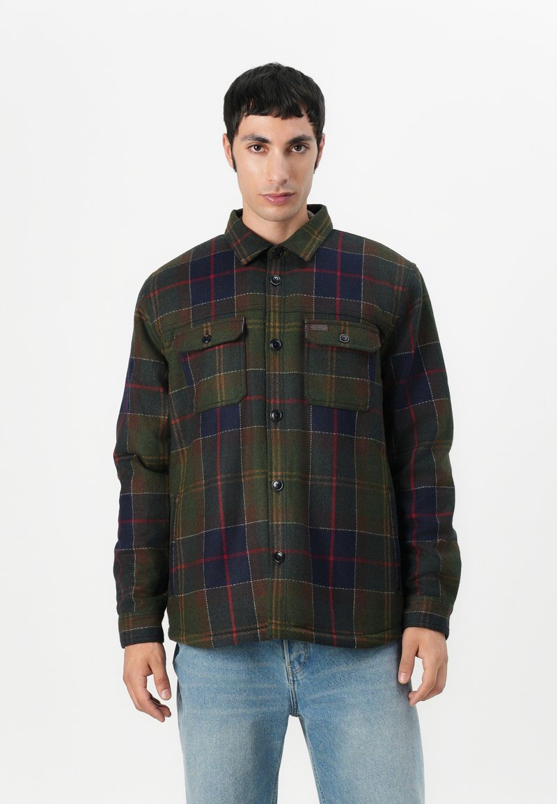 Grün und marineblau karierte Shirtjacke mit zwei Brusttaschen, schwarzen Knöpfen und Kragen. Hergestellt aus strukturiertem, warmem Stoff.