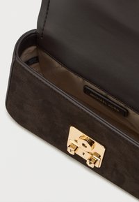 Wnętrze ciemnej skórzanej torebki o teksturowanym wykończeniu, z zamkiem w kolorze złota oraz metką z napisem "MICHAEL KORS."