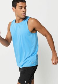 Jasnoniebieski sportowy tank top o gładkiej fakturze, okrągłym dekolcie i klinach bocznych, zestawiony z czarnymi szortami, na męskim modelu w ruchu.