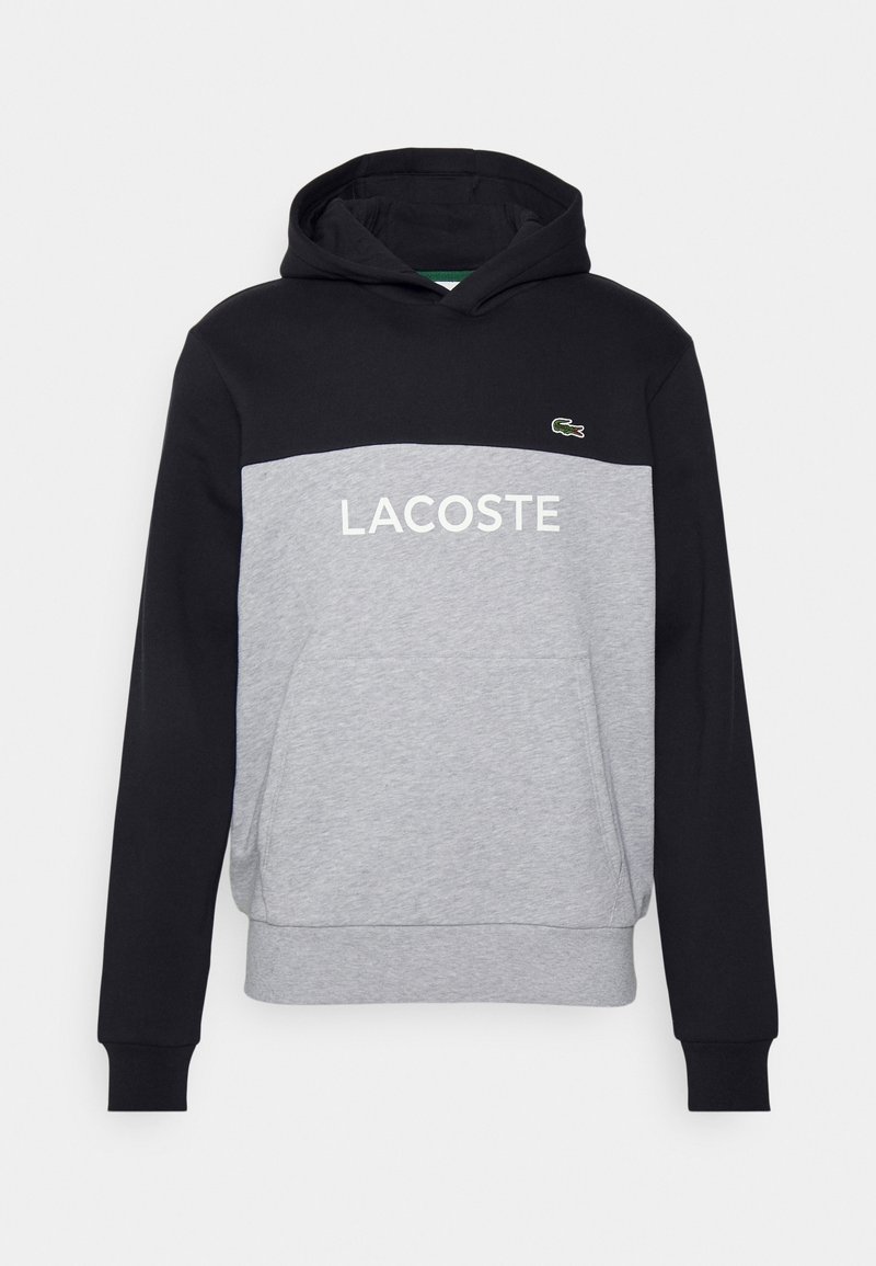 Sweat à capuche noir et gris avec poche avant, texte "LACOSTE" et petit logo crocodile vert sur la poitrine.