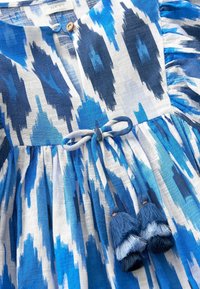 Modrá a bílá vzorovaná šaty s kulatým výstřihem, knoflíkovou aplikací, nařaseným pasem a dvěma třásněmi na lemu, vyroben�é z lehké látky.