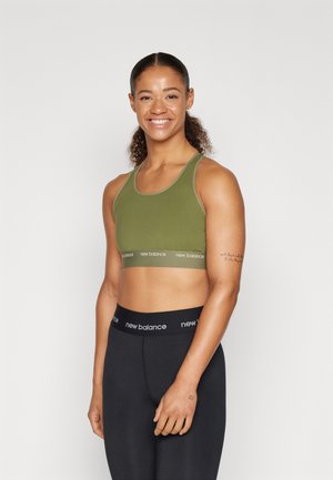 Grønn sports-bh med en kontrasterende kant som har "new balance"-logoen. Sammen med svarte leggings som fremhever en kroppsbehalende design.