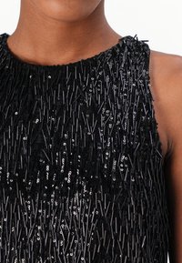 Schwarzes Kleid mit einer strukturierten Oberfläche und vertikalen Paillettensträngen. Runder Ausschnitt, ärmelloses Design und eng anliegend an den Schultern.