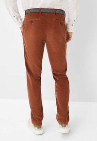 Pantalon en velours côtelé marron à coupe droite, avec des poches arrière et une ceinture grise. Assorti avec des baskets blanches, montré de dos.