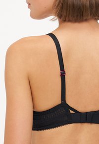 Zwarte beha met kantdetails, verstelbare bandjes en een gladde silhouet. Heeft een decoratieve band met een geschulpte rand en roze hardware.