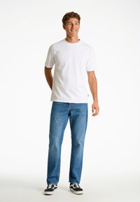 Vit bomull T-shirt, kortärmad, i kombination med blå denimjeans, avslappnad passform, och svarta sneakers med vita detaljer.