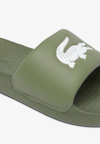 Olive green slide sandal with a smooth, matte finish, featuring a white crocodile logo on the strap and a textured footbed.